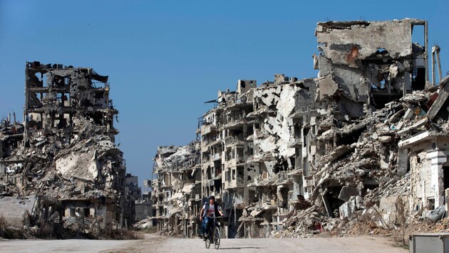 Ein Bub radelt durch die völlig zerstörte Stadt Homs. (Bild: AP)