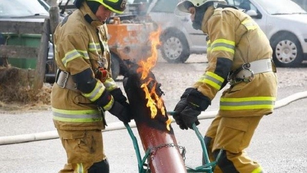 Zwei Feuerwehrmänner bringen die noch ausbrennende Gasflasche weg. (Bild: Gerhard Schiel)