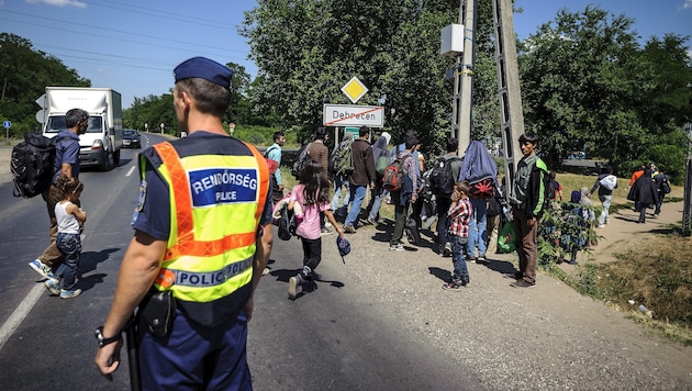 Flüchtlinge, die von einem ungarischen Grenzpolizisten eskortiert werden (Bild: APA/EPA/ZSOLT CZEGLEDI)