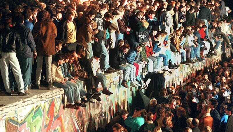 Jubelnde Menschen, die mit Wunderkerzen am 11. 11. 1989 auf der Berliner Mauer sitzen. (Bild: dpa)
